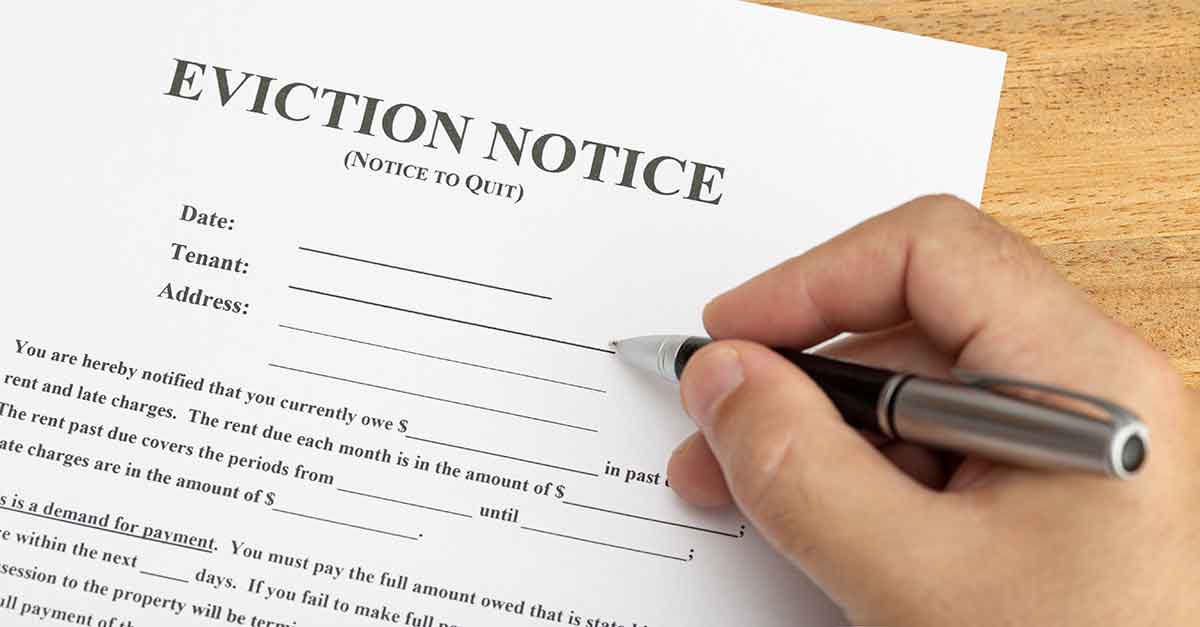 The hand of a person holds a pen ready to sign an eviction notice, which is a frequent court form among the WV Magistrate Court forms.